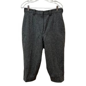 May include: Dark gray wool blend breeches, hanging on a clear plastic hanger. The pants have a high waist, belt loops, and a button and zipper closure. The knee-length pants are a classic style.