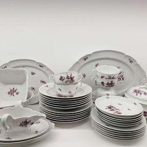 May include: A complete white porcelain dinnerware set with a purple floral pattern. The set includes plates, bowls, cups, a gravy boat, and serving platters. A classic and elegant design for formal dining.