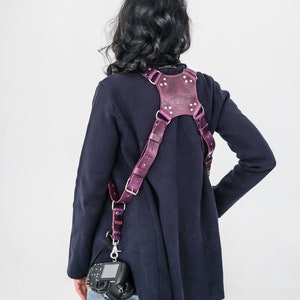 May include: A person wearing a dark blue jacket and jeans with a purple leather camera strap and a black camera attached.