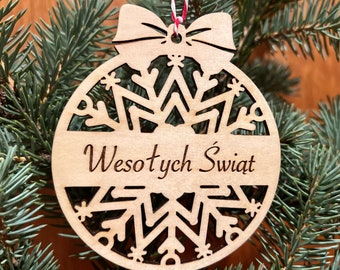 May include: A wooden Christmas ornament shaped like a snowflake with the text "Wesołych Świąt" in the center. The ornament is hanging on a Christmas tree.