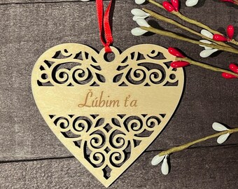 May include: A wooden heart-shaped ornament with a decorative cut-out design. The ornament is painted in a light wood color and has the text "Lúbim t'a" inscribed on it.