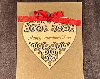 May include: A brown card with a red ribbon tied around a wooden heart cutout. The heart has a decorative design and the text "Happy Valentine's Day" inside.