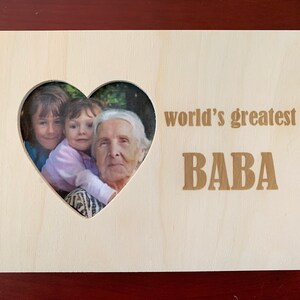 Puede incluir: Un marco de fotos de madera con un recorte en forma de corazón para una foto. El marco tiene el texto "world's greatest BABA" grabado.