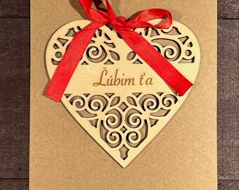 May include: A brown card with a red ribbon tied around a wooden heart cutout. The heart has a decorative design and the text "Lubim t'a" is inscribed on it.