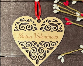 May include: A wooden heart-shaped ornament with a decorative cut-out design. The ornament is painted brown and has the text "Sretno Valentinovo" written in a cursive font.