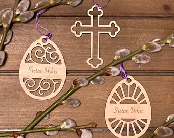 May include: Three wooden Easter decorations with a willow branch. Two of the decorations are egg-shaped with the text "Sretan Uskrs" and intricate cut-out designs. The third decoration is a cross with a simple design.