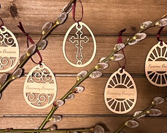 May include: Five wooden Easter egg ornaments with intricate designs and the text "Христос Воскресе" (Christ is Risen) in Cyrillic script. The ornaments are hanging from a branch with fuzzy buds.