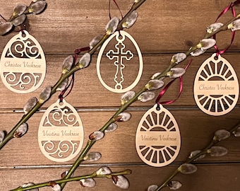 May include: Five wooden Easter egg ornaments with intricate designs and the text "Christos Voskrese" and "Voistinu Voskrese" in a cursive font. The ornaments are hanging from willow branches.