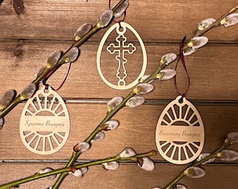 May include: Three wooden Easter egg ornaments with intricate designs. The top ornament features a cross, the middle ornament says "Христос Воскресе" (Christ is Risen), and the bottom ornament says "Воистину Воскресе" (Truly He is Risen).