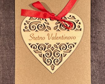 May include: A brown card with a wooden heart cutout attached with a red ribbon. The heart has a decorative design and the text "Sretno Valentinovo" in the center.