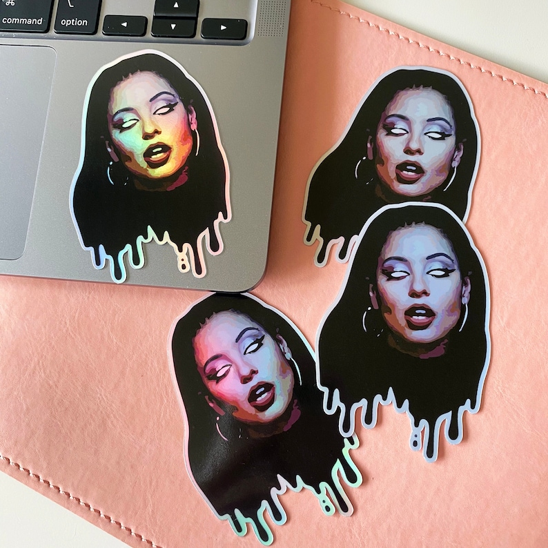 May include: Three holographic stickers featuring a woman with long black hair and a dripping effect. The woman's face is partially obscured by her hair, and she is wearing large hoop earrings. The stickers are on a pink surface.