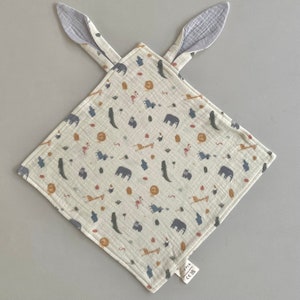 May include: A white muslin baby security blanket with a light blue and brown animal print. The blanket has two attached ears and a label that reads "101K CE EN71".