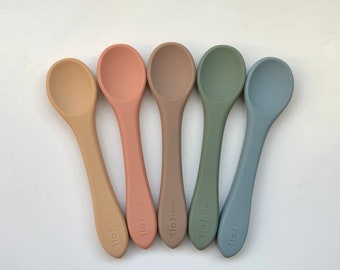 May include: Five silicone baby spoons in different colors: beige, pink, brown, green, and blue. Each spoon has the text "mini folk" printed on the handle.