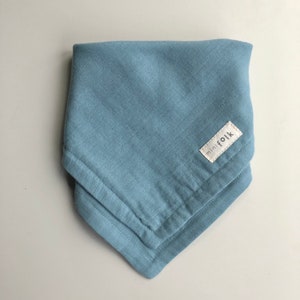Peut inclure: Un bandana en mousseline pour bébé de couleur bleu clair avec une étiquette blanche sur laquelle est inscrit "mini folk".