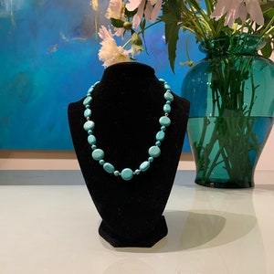 May include: A turquoise blue necklace made of round wooden beads on a black velvet display stand.
