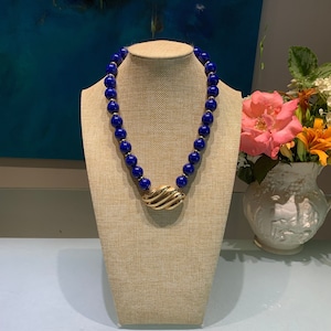 May include: A gold necklace with a large, textured, gold pendant and blue beads.