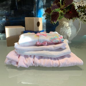 May include: A stack of pink and white baby clothes with a floral design. The clothes are folded neatly and are ready to be worn.