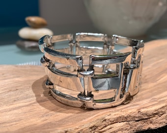 May include: A silver bracelet with a geometric design. The bracelet is made of interlocking metal pieces that create a cage-like effect.
