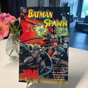 May include: A Batman Spawn War Devil comic book featuring a colorful cover illustration of Batman and Spawn. The title text is displayed in bold yellow and green lettering, with the names of creators Doug Moench, Chuck Dixon, Alan Grant, and Klaus Janson printed in white at the bottom right corner.