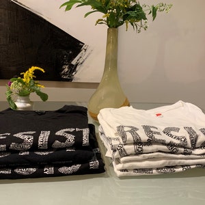 May include: A stack of black t-shirts with the word "RESIST" spelled out in white letters, and a stack of white t-shirts with the word "RESIST" spelled out in black letters. The shirts are made of a soft, comfortable material and feature a variety of words related to social justice and resistance.
