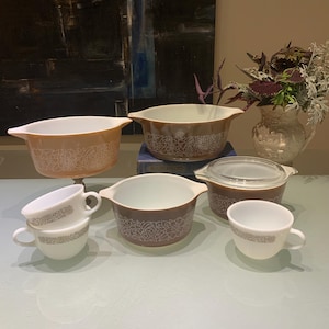 May include: A set of vintage brown and white casserole dishes with a floral pattern. The set includes a large casserole dish with a lid, a smaller casserole dish, and two small bowls.