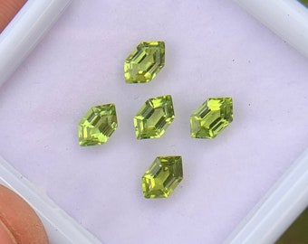 May include: Five green gemstones in a square white box. The gemstones are cut in a rectangular shape with pointed ends.