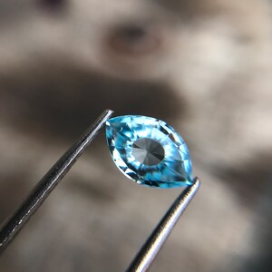 May include: A light blue marquise-shaped gemstone with a faceted design. The gemstone is held in tweezers.