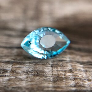 May include: A light blue aquamarine gemstone with a marquise cut. The gemstone is faceted and has a brilliant shine.