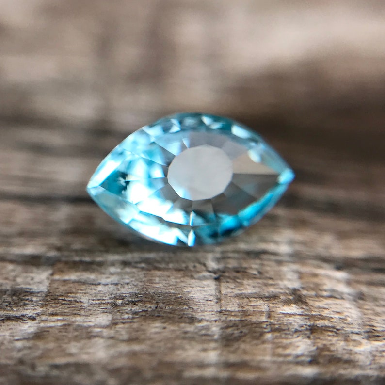 May include: A light blue aquamarine gemstone with a marquise cut. The gemstone is faceted and has a brilliant shine.