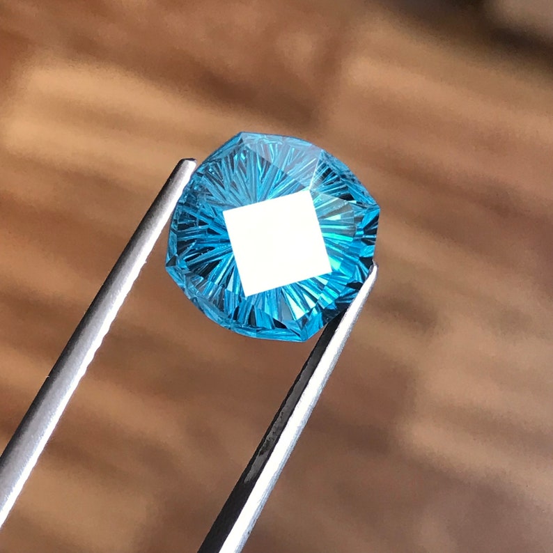 Puede incluir: Una piedra preciosa azul con un dise&ntilde;o facetado en forma de estrella. La piedra preciosa se sostiene con unas pinzas.