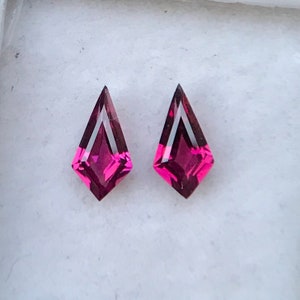 May include: Two pink gemstone earrings with a kite shape and a faceted cut.