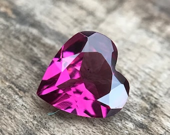 Può includere: Una gemma sfaccettata a forma di cuore con una tonalità rosa intenso. La gemma è posizionata su uno sfondo di legno rustico.
