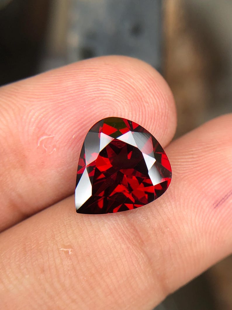 May include: A deep red heart-shaped gemstone with a faceted cut.