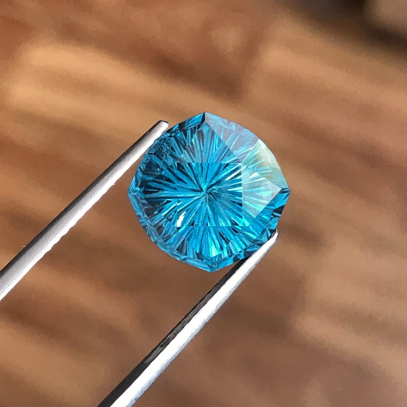 Puede incluir: Una piedra preciosa azul con un patr&oacute;n de estrella, sostenida por unas pinzas. La piedra preciosa est&aacute; facetada y tiene una forma hexagonal.