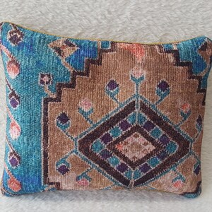 May include: A small, decorative cushion with a blue, brown and pink patterned design. The pattern is reminiscent of a traditional rug.