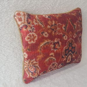 May include: Red and orange patterned cushion with a gold trim. The cushion has a floral design with intricate details.
