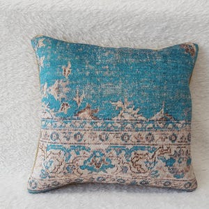 May include: A turquoise blue cushion with a cream and brown patterned design. The cushion has a traditional, ornate pattern.