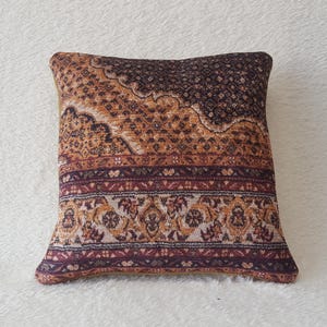 May include: A decorative cushion with a brown, orange and white patterned design. The cushion is square shaped and made from a soft, plush fabric.