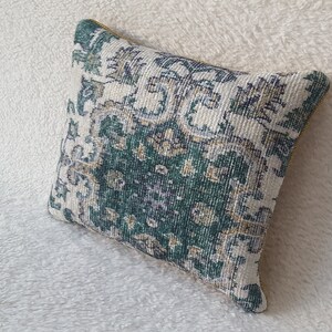 Könnte beinhalten: Ein Dekokissen mit einem gemusterten Design in Grün, Weiß und Beige. Das Kissen hat einen goldenen Reißverschluss und ist aus einem weichen, strukturierten Stoff gefertigt.