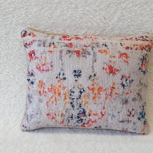 May include: A decorative throw pillow with a white background and a colorful, abstract pattern in shades of orange, pink, blue, and gray.