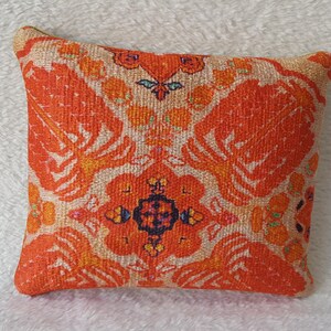 May include: Orange and white cushion with a floral pattern. The cushion is square shaped and made from a soft, textured fabric.
