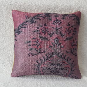 May include: A pink cushion with a black floral pattern. The cushion is made of a soft, textured fabric.