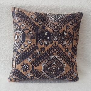 Könnte beinhalten: Ein quadratisches Kissen mit einem geometrischen Muster in Braun, Schwarz und Weiß. Das Kissen hat in der Mitte eine Diamantform mit einem floralen Design.