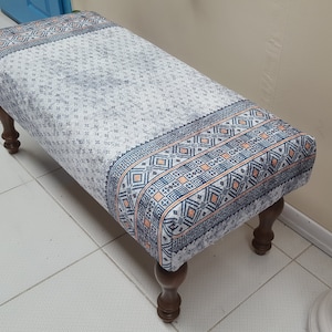 May include: A white and blue patterned bench with wooden legs. The bench has a geometric design with orange accents.