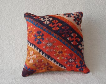 May include: A decorative pillow with a colorful geometric pattern in shades of red, orange, blue, and black. The pillow is made of a soft, woven fabric and has a square shape.