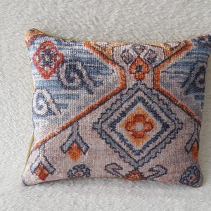 May include: A decorative cushion with a colourful geometric pattern in shades of blue, orange, and beige. The cushion is square shaped and has a soft, plush texture.