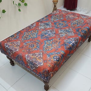 May include: A red, blue, and white patterned ottoman with wooden legs. The ottoman is sitting on a white tiled floor.