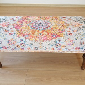 Puede incluir: Un otomano con estampado colorido sobre fondo blanco y patas de madera. El estampado presenta un gran medall&oacute;n central con dise&ntilde;os florales y geom&eacute;tricos en tonos rojos, amarillos, azules y verdes.