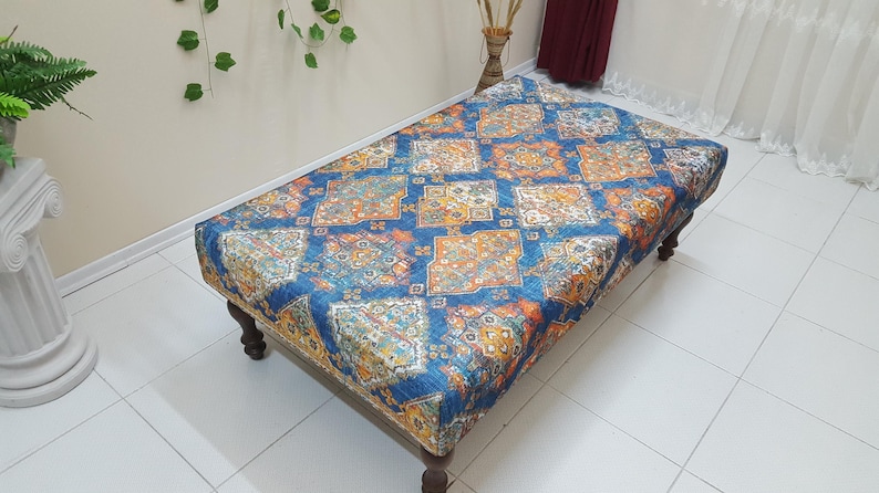 Peut inclure: Un ottoman bleu et orange &agrave; motifs avec des pieds en bois. L'ottoman a un design traditionnel avec des d&eacute;tails complexes.