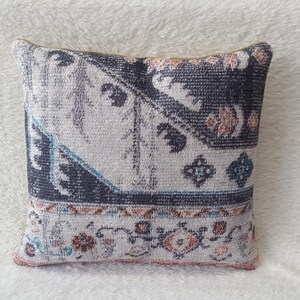 May include: A decorative throw pillow with a blue, white and pink patterned design. The pillow has a geometric pattern with a border of floral motifs.